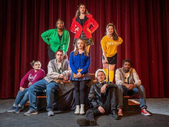 The full cast of Heathers The Musical. They are in vivid colored clothing with sad expressions.