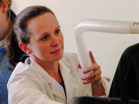 Photo of professor Jennifer McKenzie in a lab coat holding a breathing tube in the lab.