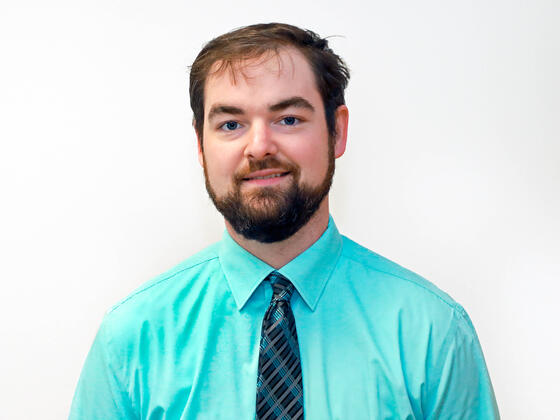 A staff member of McDaniel College in an aqua shirt in front of a white wall.