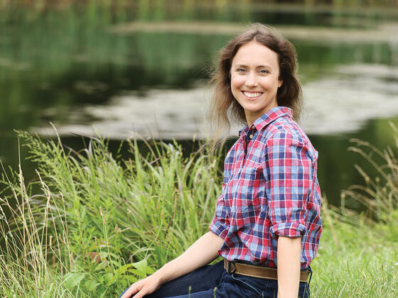 Photo of professor Margaret Christie sitting on the bank of a lake. 