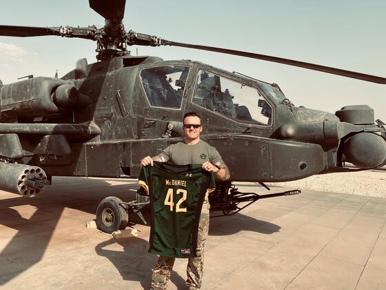 Nick Giusti holds up a McDaniel football jersey in front of a helicopter while stationed in Syria.