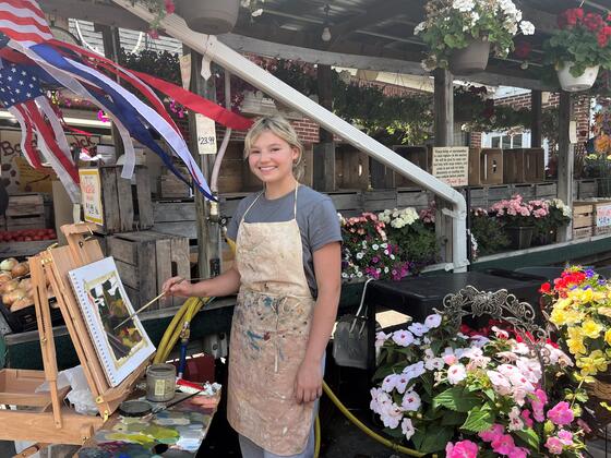 Student Mandy Smith painting on an easel at Baugher's local market stand.