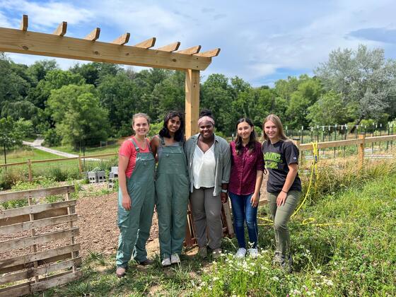 Four students pose with professor Elly Engle in front of a vegetable garden at the McDaniel Environmental Center.