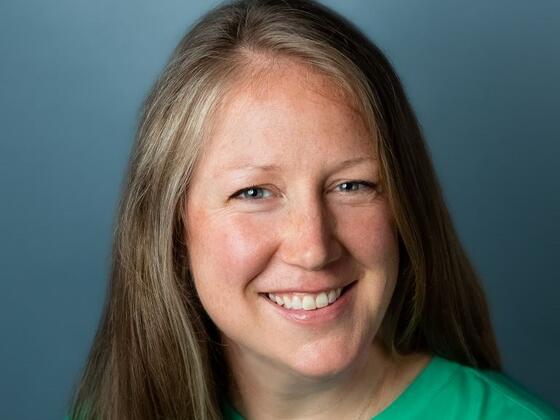 Headshot of Lauren Stevens in a green shirt on a dark blue background.