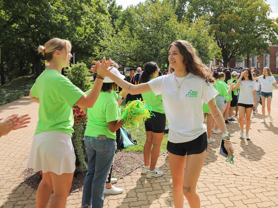 A first-year, female student in a white t-shirt high fives with a female peer mentor in a green t-shirt.