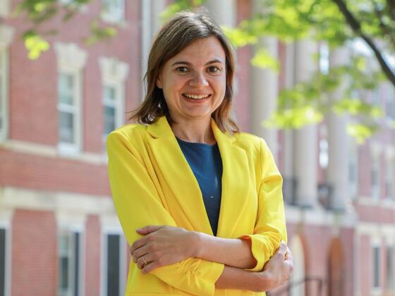 Photo of a white female in a bright yellow suit jacket standing in front of a brick academic building.