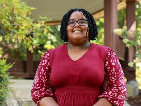 Photo of a Black female wearing a red flower pattern dress in front of a gazebo.