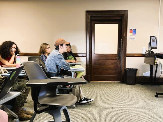 A woman speaks to students seated in a classroom.