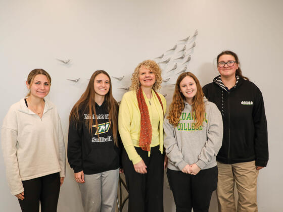 Five women stand together for a photo in front of a white wall with bird decals.