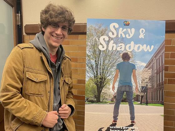 A man stands next to a poster reading "Sky and Shadow."