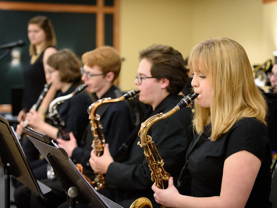 Students sit in a row playing saxophones.