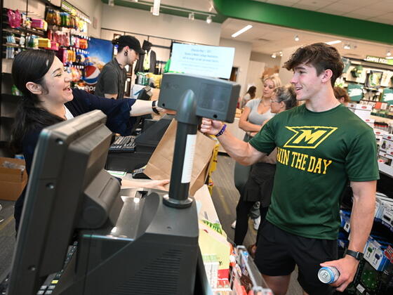 Photo of a male student buying an item at the sales counter in the cmapus bookstore, and female salesperson on the other side of the counter.