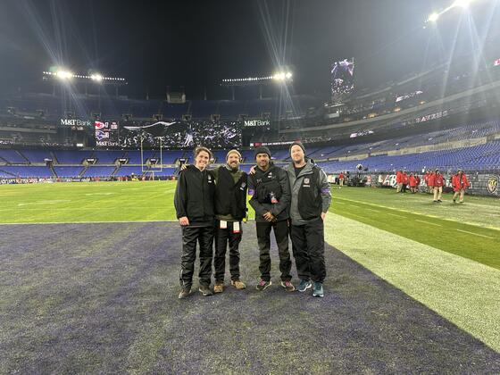 Four people stand on the Baltimore Ravens stadium end zone.