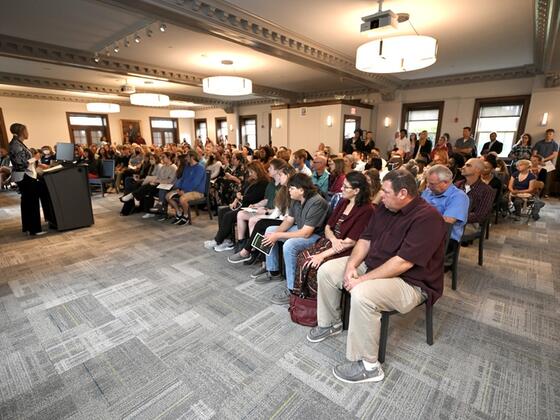 An audience sits in front of President Jasken at a podium.