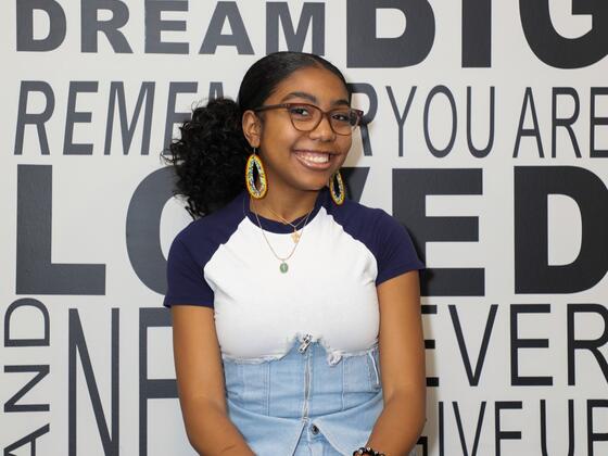 A female student sits in front of a wall with aspirational words on it like "Dream Big."