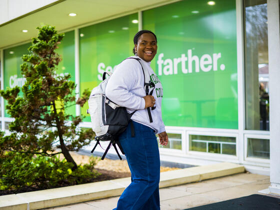 A student smiles to the side while walking with a backpack on their shoulder.