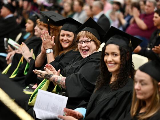 Group of students in commencement regalia sit in chairs