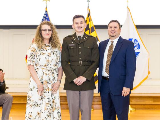 A cadet poses on stage between his mother and father.