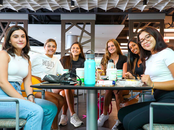 A group of female students sits at a table and smiles toward the camera.