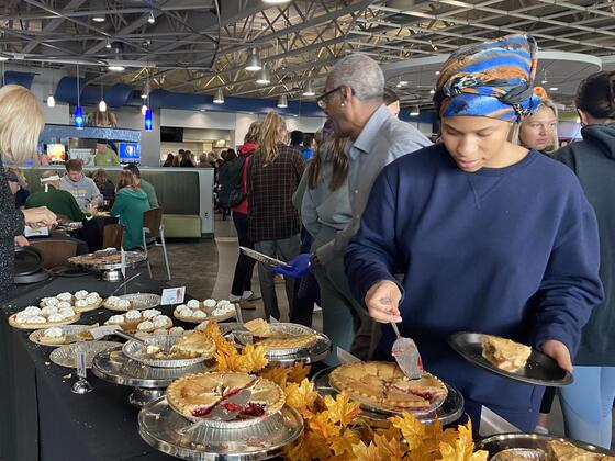 A student fills a plate at a table with Thanksgiving pies on it.