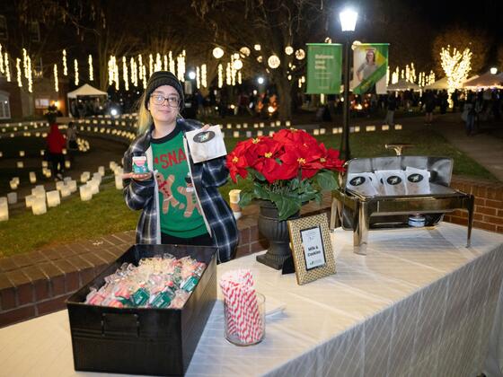 A member of AVI wears a holiday sweater while posing by a table with milk and cookies on it.
