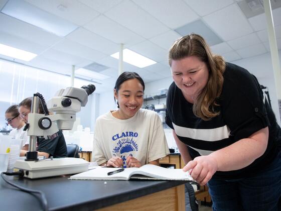 A McDaniel research student and professor look at a notebook next to a microscope.