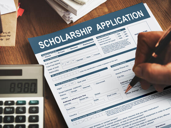 A hand fills out a form that says "Scholarship Application"