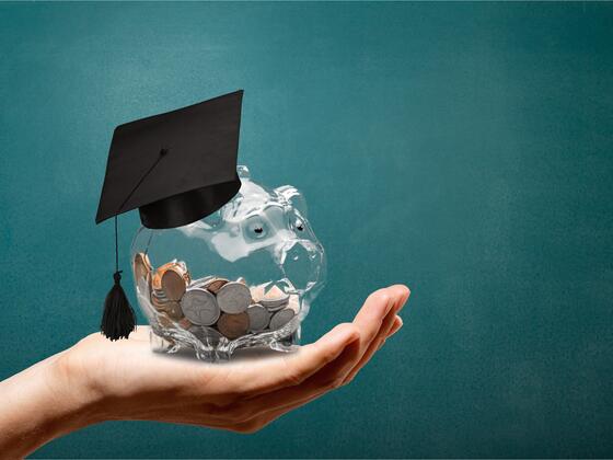 A hand holds a piggy bank with coins inside