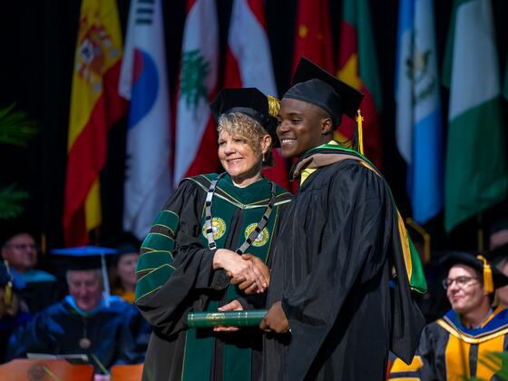 McDaniel President Julia Jasken shakes hands with a student in graduation regalia while passing along his diploma.