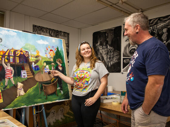 Student shows professor a painting of a carnival scene