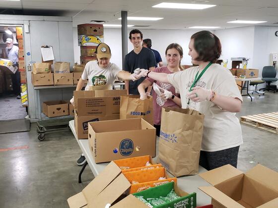 A group of student volunteers fill cardboard boxes with food.