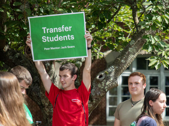 student wearing red shirt holding up sign that says "Transfer Students"