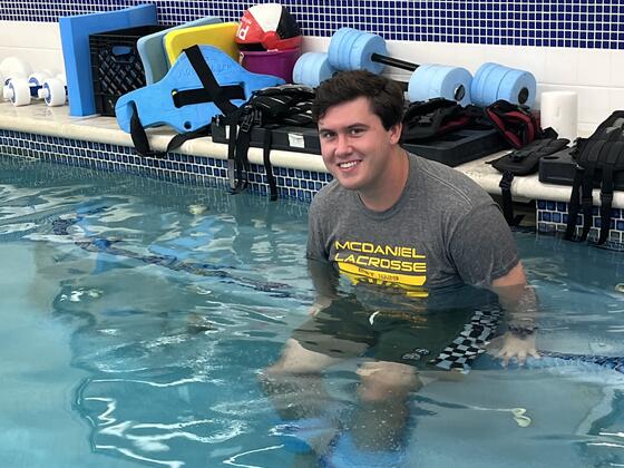 A white man in a "McDaniel Lacrosse" T-shirt sits in a pool.