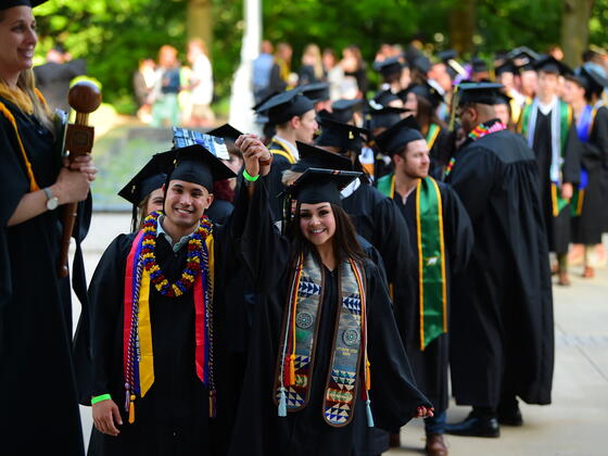 Students in graduation regalia walk in a line