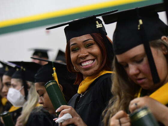 A female student in regalia smiles and holds up her degree tube at the commencement ceremony.