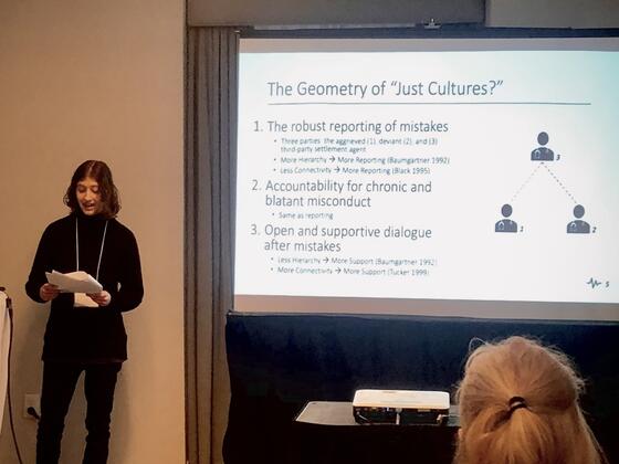 Student Kaiya Mayhew stands next to a large presentation screen at a sociology conference.