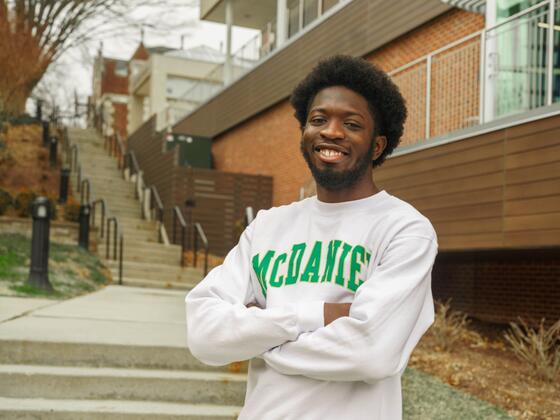 Olanrewaju Oluwaseyi Abayomi stands outside in front of a staircase with his arms crossed, wearing a McDaniel College sweatshirt.