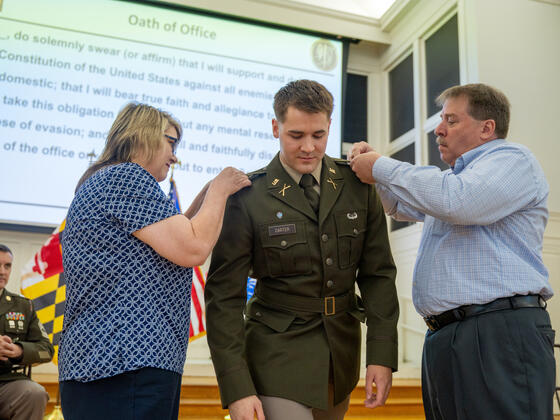 Joshua Carter in uniform while his parents add pins to his shoulders.