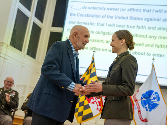 Jolie Gray, in uniform, shakes hands with her grandfather on satge at Commissioning.