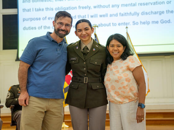 Elana Petrone, in uniform, smiles with her parents on stage at Commissioning.