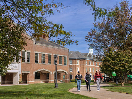 Three students walking down a pathway in front of Merritt Hall in the springtime.