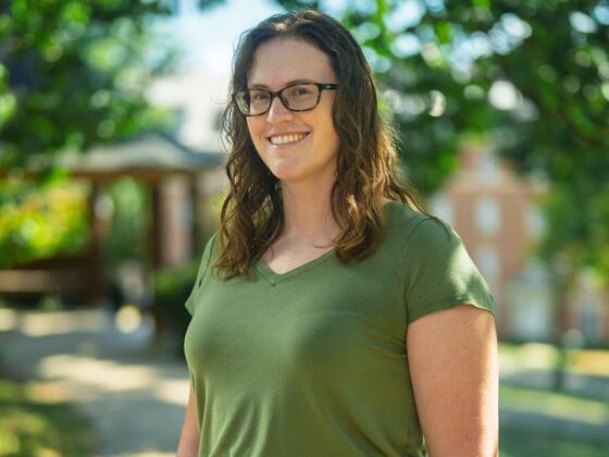 Christine Conte stands outside in front of a gazebo while wearing a green shirt and tan pants.