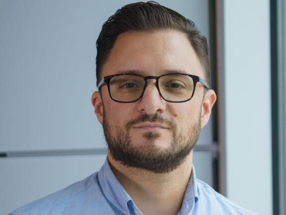 Headshot of Christopher Palmore wearing a blue button-up shirt and black-rimmed glasses.