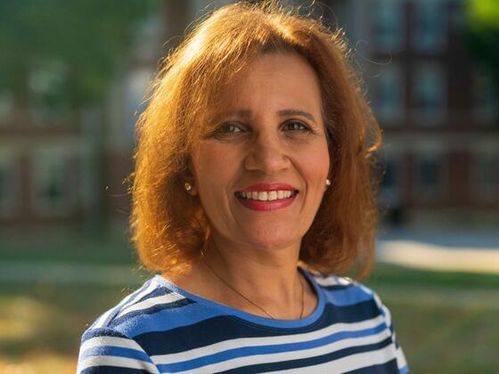 Dina Rady smiles outside of a campus building while wearing a blue and white striped shirt.