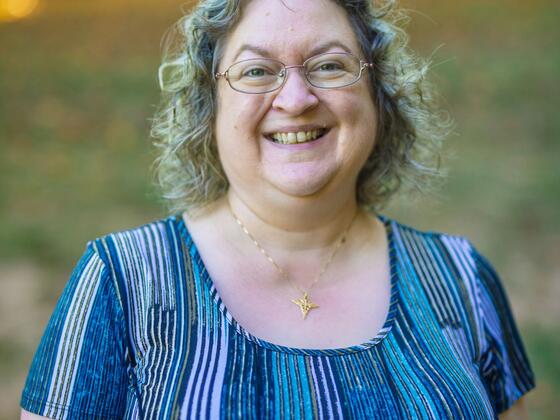 Laura Steakin smiles while standing outside and wearing a blue striped shirt.