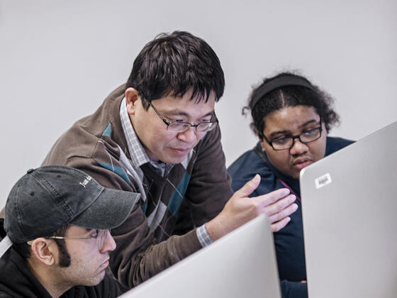An instructor gestures at a computer in front of two students.