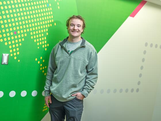 A male student stands in front of a green patterned wall.