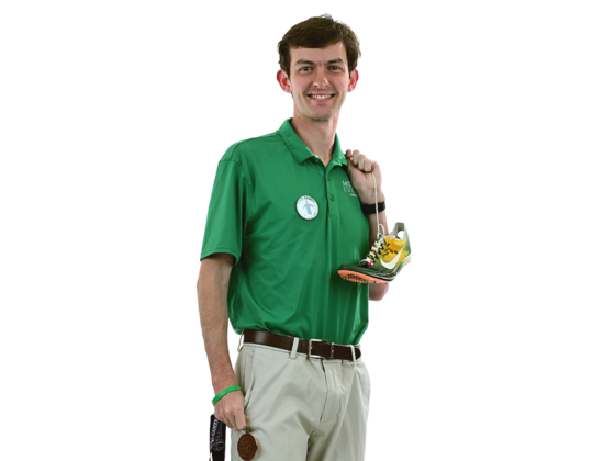 A male student in a McDaniel polo holds a gold medal and track shoes.