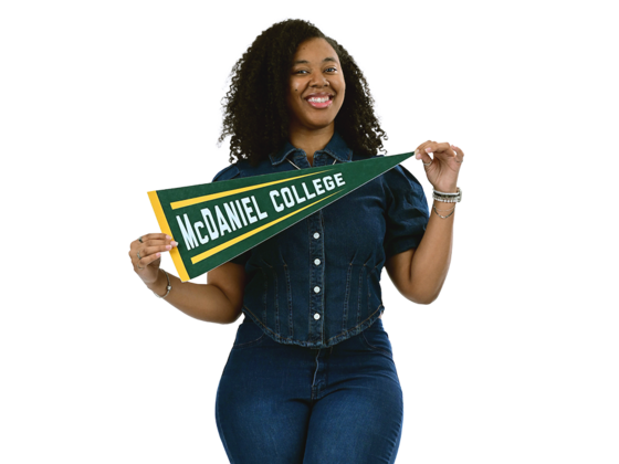 A female student wearing a denim outfit poses with a McDaniel College pennant.