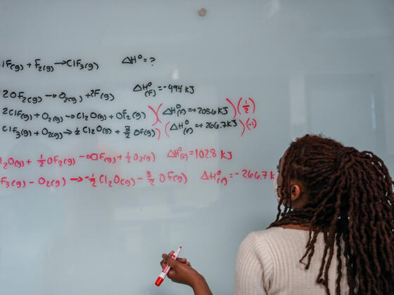 A student writes an equation on a whiteboard.